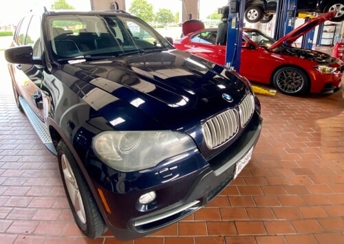 EurAuto Shop in Plano Tx, bmw diesel repair and service on a navy blue and red BMW sedan with hood open to perform vehicle maintenance services to it in the shop bay