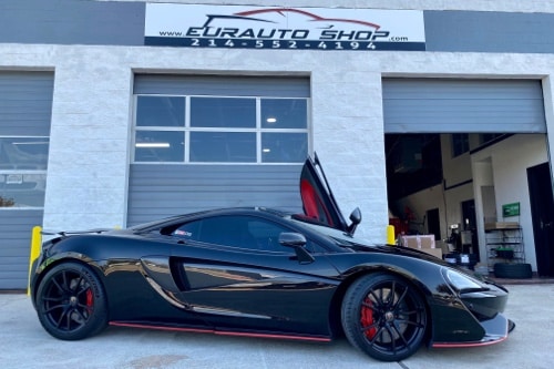 EurAuto Shop in Plano Tx, Mclaren auto repair and service; black with red accessories and lambo style doors mclaren that was serviced at the shop is pictured outside of office door at the shop with driver side door opened