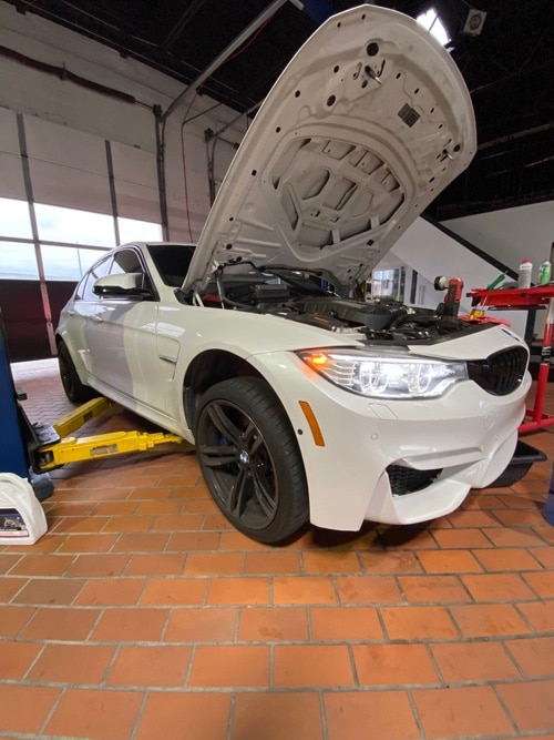 EurAuto Shop in Plano Tx, has a white BMW sedan with hood open to perform vehicle maintenance services to it