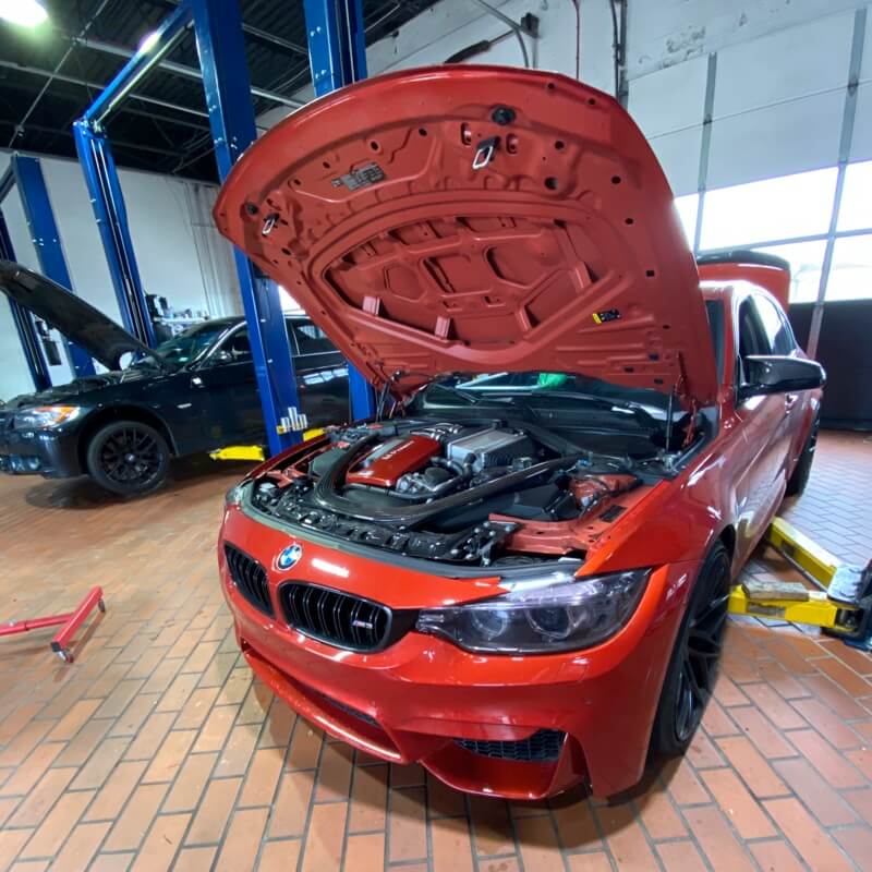 Repairing BMW Valve Cover Oil Leaks at EurAuto Shop in Plano Tx, image of red bmw with hood open inside bay of shop