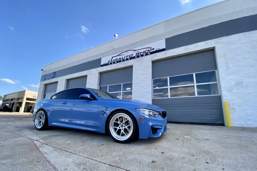 Sharpen Handling With a BMW Coilover Conversion, EurAuto Shop in Plano Tx.; blue bmw parked vertically outside of EurAuto shop bay area doors that came in for coilover services