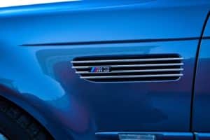 Lowering the Suspension For Improved Handling on BMW M3 closeup image of BMW M3 emblem on side of blue sedan