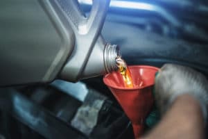Regular Oil Changes Are Key To Maintaining BMW Performance In Plano Tx with EurAuto Shop closeup image of mechanic wearing dirty white gloves holding red funnel while pouring oil into car engine