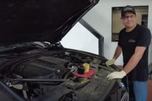 Can You Afford a Cheap Oil Filter? with EurAuto Shop in Plano TX, image of shop mechanic Jonathan standing in front of BMW N55 car with cheap oil filter and OEM filter resting on engine of car in shop