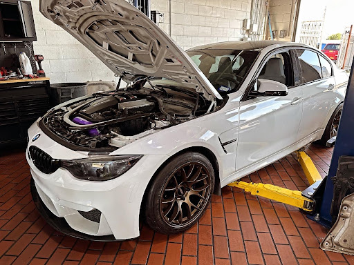 BMW M-Series maintenance near me with EurAuto Shop in Plano, TX. Image of newer model white BMW M series car with hood up on lift in shop for maintenance services.