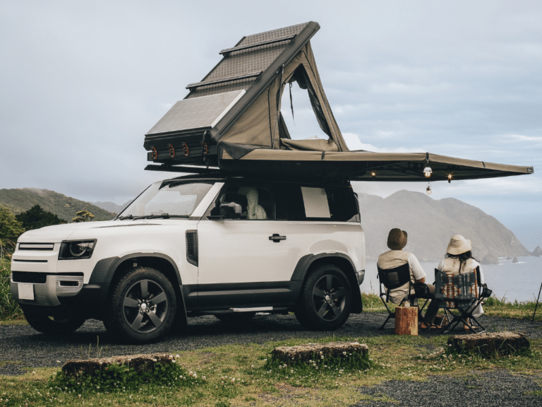 Land Rover Defender reliability insights by EurAuto Shop, Plano, TX. Image shows a white Land Rover Defender with a roof tent setup on a scenic cliffside, highlighting the vehicle's off-road capabilities and suitability for adventurous outdoor activities.