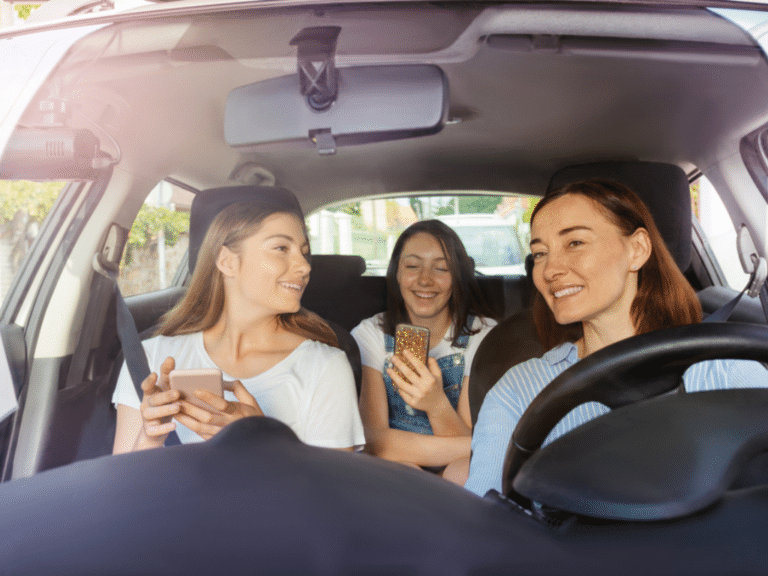 Summer road trip preparation by EurAuto Shop, Plano, TX. Image shows a mother and her teenage daughters inside a car, smiling and using their smartphones, emphasizing the importance of a well-maintained A/C system for a comfortable and enjoyable journey.