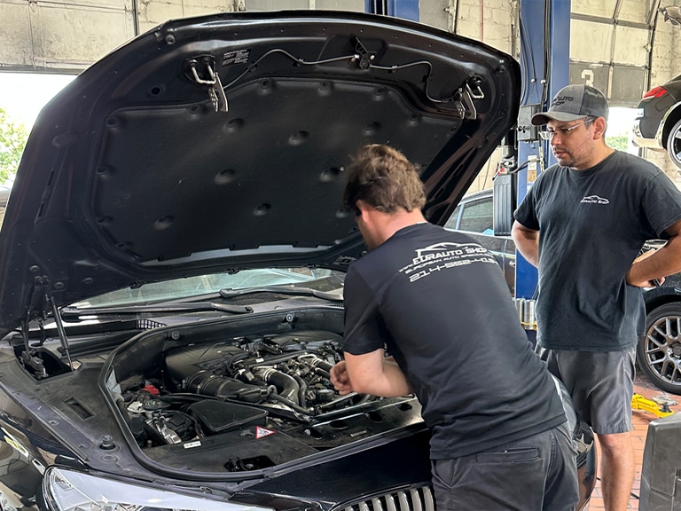 Failed PCV Valve on BMW in Plano, TX with EurAuto Shop, independent BMW repair shop. Image of two male EurAuto Shop mechanics performing PCV repair on a black BMW that came in the shop for repairs.