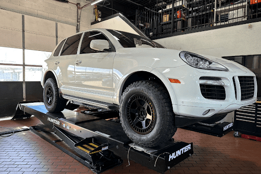 Wheel alignment checks in Plano, TX with EurAuto Shop for Porsche, BMW, Mercedes, Jaguar, Land Rover and more. Image of white Porsche SUV with modified wheels on the hunter wheel alignment machine in the shop for a check.