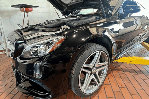 Get Your European Car Holiday-Travel Ready at EurAuto Shop ion Plano, TX. Image of newer black mercedes on lift in the shop with hood open and fluid exchange machine next to it for a routine oil change.