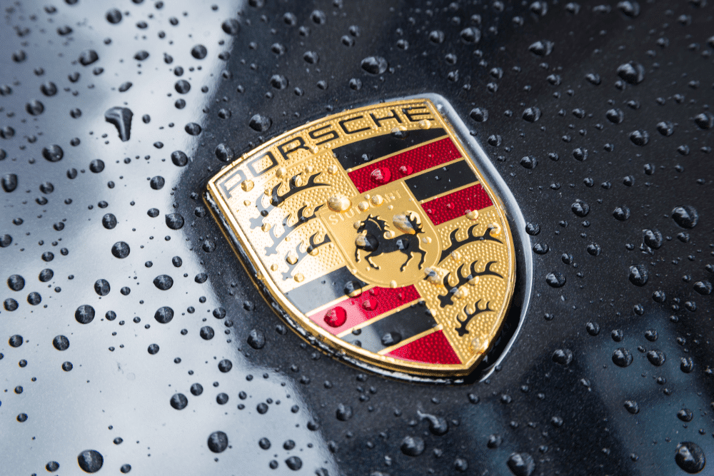 porsche cayenne vs porsche macan, european auto repair in Plano, TX at EurAuto Shop. Close-up of a Porsche logo on a black car hood covered in water droplets.