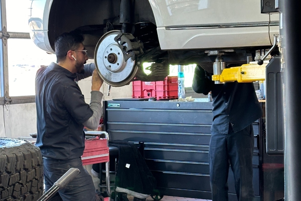 Two technicians performing brake repair on a white vehicle lifted in a professional auto shop in Plano, TX at EurAuto Shop. Brake Repair in Plano TX At EurAuto Shop